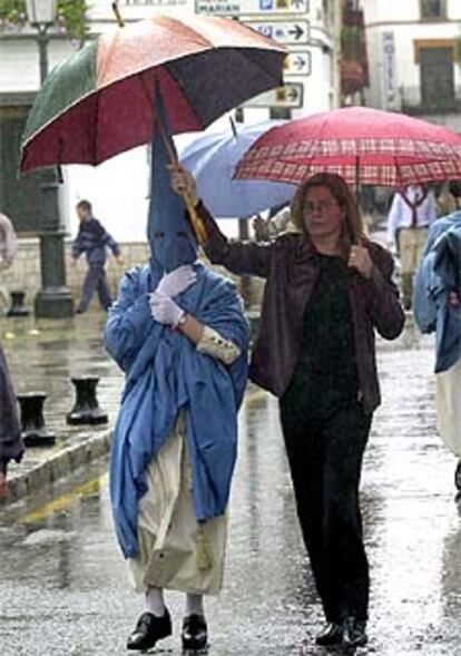 Una mujer protege con un paraguas a un nazareno en Sevilla.