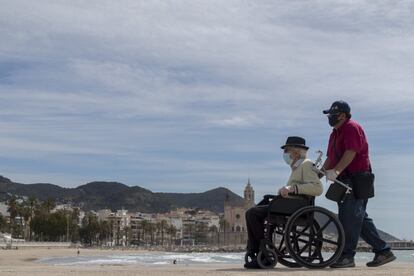 Un hombre pasea con una persona dependiente junto a la playa de Sitges, este sábado. 