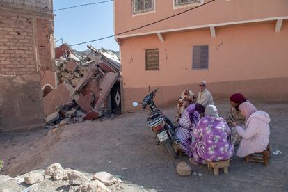 Varias personas sentadas en una calle junto a los restos de un edificio colapsado en Marraquech. 