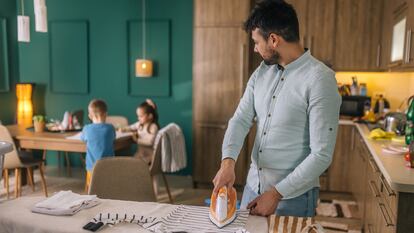 Un padre plancha la ropa de sus hijos.