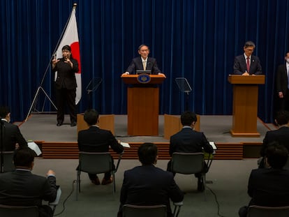 El primer ministro japonés Yoshihide Suga, en el centro, y el responsable del gobierno japonés sobre la pandemia, Shigeru Omi, a la derecha, en una rueda de prensa para actualizar los datos de contagios y medidas en el país nipón