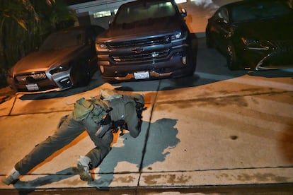 An officer checks under cars at a house suspected of harboring drug traffickers, in California.