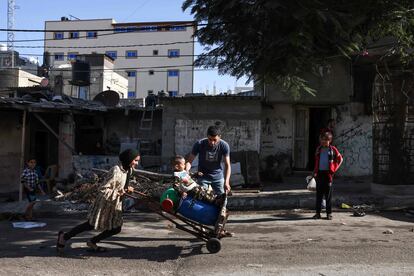 Una joven empuja un carro con bidones llenos de agua mientras un niño se mantiene sobre ellos, este viernes en Rafah.