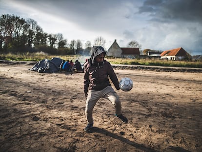 Un joven juega al fútbol en un campamento improvisado en la periferia de Calais (Francia), donde migrantes de diversas nacionalidades aguardan para intentar alcanzar el Reino Unido.