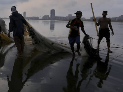 Pie de Foto: Un grupo de pescadores paquistaníes arrastran sus redes en una playa de Karachi, Pakistán