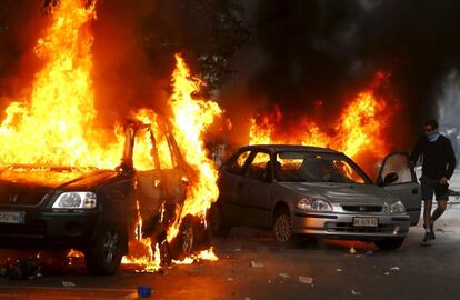 Un hombre intenta salvar su coche del incendio que afecta a otros dos vehiculos, tras el ataque de unos manifestantes, este viernes en Milán.