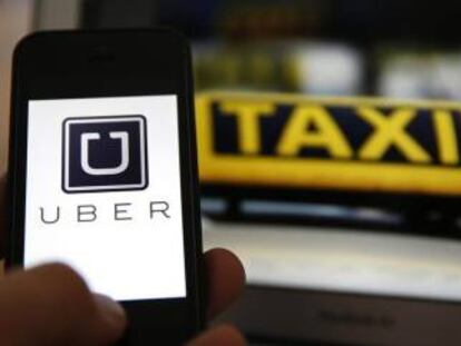 Logo de Uber en un móvil junto a un taxi.