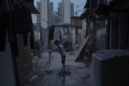 Un niño de cinco años juega fuera de su pequeña casa, hecha de hormigón y metal corrugado, en la terraza de un bloque de apartamentos. Vive en una choza ilegal en la azotea, al lado de una urbanización pública, que se ve al fondo.