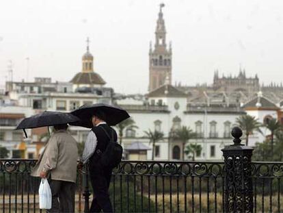 Dos transeúntes cruzan bajo la lluvia el puente de Triana, en Sevilla.