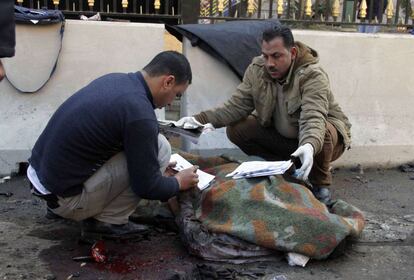 Una segunda explosión, tres horas después, ha causado la muerte de un policía y heridas a una quincena de personas cerca de una estación de metro de la capital. En la imagen, dos forenses junto al cadáver de una de las víctimas del atentado de la sede de la policía en El Cairo (Egipto).