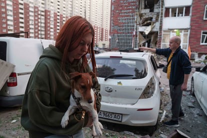 Una mujer sostiene a su perro mientras, a pocos metros, un hombre aparta escombros de un vehículo dañado tras un ataque ruso sobre Kiev, este martes