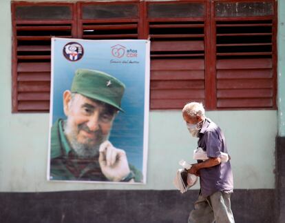 Un hombre con mascarilla camina frente a una imagen de Fidel Castro en una calle de La Habana, Cuba