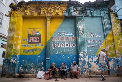 Personas sentadas junto a un muro con lemas políticos en La Habana, Cuba, el pasado 23 de diciembre.