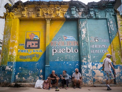 Personas sentadas junto a un muro con lemas políticos en La Habana, Cuba, el pasado 23 de diciembre.