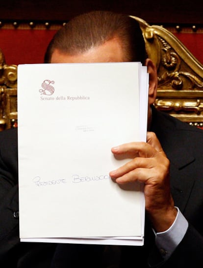 El primer ministro italiano, Silvio Berlusconi, se tapa la cara con una carpeta durante la sesión del Senado, donde ha superado el voto de confianza.