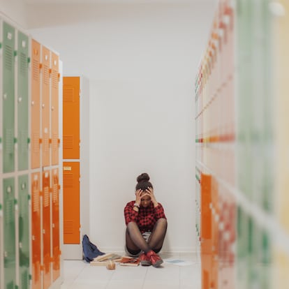 Sad student girl sitting in the floor in school locker room. Concept of bullying and depression at teenagers.