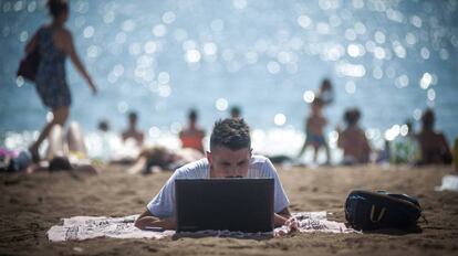 Una persona utiliza su ordenador en la playa de la Barceloneta. 