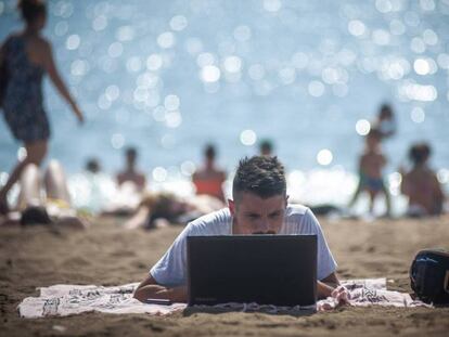 Una persona utiliza su ordenador en la playa de la Barceloneta. 
