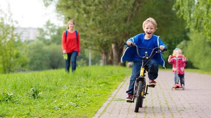 Dos niños juegan en un parque con una bicicleta y un patinete.