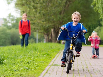 Dos niños juegan en un parque con una bicicleta y un patinete.