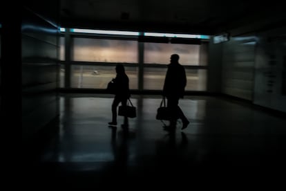 Dos personas caminan por un pasillo en penumbras del aeropuerto internacional 'Simón Bolívar' ubicado en Maiquetia, que sirve a la ciudad de Caracas (Venezuela). 
