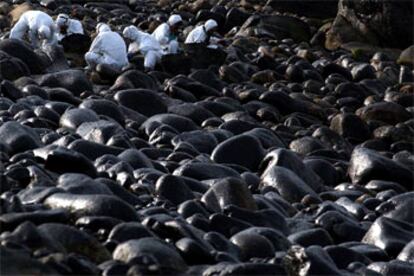 Un grupo de voluntarios limpiaba ayer de chapapote las rocas manchadas con fuel procedente del <i>Prestige</i> en la costa de Muxía.