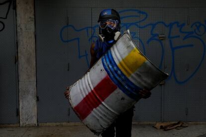 Um manifestante ergue seu escudo fabricado com um tonel de metal. ‘Luto pela liberdade de expressão’.