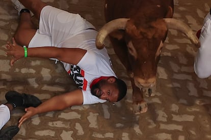 Un corredor cae al paso de uno de los toros en el callejón de entrada a la plaza de toros de Pamplona.