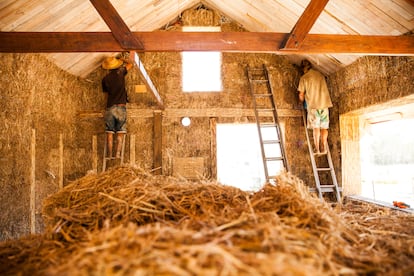 Dos personas construyendo una casa con fardos de paja utilizando métodos de construcción naturales.