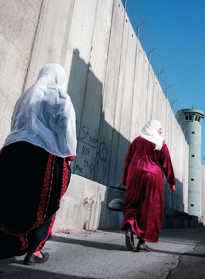 Dos mujeres palestinas pasan frente al muro de Belén levantado por Israel.  La Corte Internacional declaró en su opinión consultiva de julio de 2004 que el muro viola el derecho internacional. Pese a ello, Israel continúo su construcción.