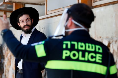 Un policía con mascarilla desaloja a un ultraortodoxo de un centro de estudios judío.