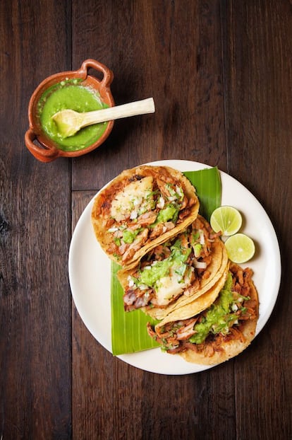 <p><i>Tacos de cerdo marinado en pasta de chile. Región: Distrito Federal</i></p><p><b> Ingredientes</b></p><p> Para 6 personas: 5 chiles guajillo sin membranas y despepitados, 5 cucharadas de vinagre de sidra, 3 dientes de ajo pelados, una pizca de comino molido, 2 clavos, 2 cucharadas de zumo de piña (opcional) y un poco más para servir, una pierna o cuarto trasero de cerdo de 500 gramos cortado en rodajas finas, 2-3 cucharadas de aceite de maíz, una cebolla grande en rodajas finas, sal marina. Para servir: 12 tortillas pequeñas, media piña pelada cortada en cuartos y después en rodajas sin el corazón, una cebolla pequeña picada fina, 4 cucharadas de cilantro picado fino y la salsa al gusto.</p><p><b> Preparación</b></p><p><i> Elaboración de 30 minutos, más 5 horas para marinar. Cocción: 35 minutos. </i></p><p> 1. Colocar los chiles en una cazuela, añadir el vinagre y cocerlos 15 minutos a fuego lento, hasta que estén tiernos. Agregar el ajo, el comino y los clavos, pasar la mezcla a un robot de cocina o una batidora y triturarlos hasta obtener una pasta. Añadir más vinagre, si fuera necesario, y el zumo de piña (opcional) y colar. 2. Pasar la pasta a una cazuela y cocerla a fuego lento 10 minutos, removiendo constantemente para evitar que se pegue. Retirarla del fuego y dejar que se enfríe. 3. Extender una fina capa de pasta de chile sobre las rodajas de carne. Apilarlas en un plato, cubrirlas con film transparente y dejarlas marinar en el frigorífico 5 horas o toda la noche. 4. Calentar el aceite en una sartén. Echar las rodajas de cerdo y freírlas 2 minutos, darles la vuelta y freír otros 2 minutos, hasta que estén medio hechas. Retirar la carne de la sartén, cortarla en trozos y devolverla a la sartén. Añadir la cebolla y freírla 3 minutos. 5. Pasar la carne a una fuente de servir. Freír las tortillas en la sartén, de una en una, de 20 a 30 segundos por cada lado. Retirarlas y dejarlas escurrir sobre papel de cocina. 6. Repartir la carne sobre las tortillas y añadir las rodajas de piña, la cebolla, el cilantro y, por último, la salsa. Servirlas de inmediato.</p>