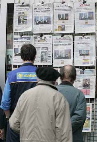 Tres personas leen portadas en un quiosco en San Sebastián.