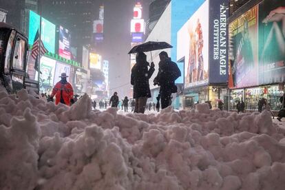 Varias personas esperan en Times Square junto a un montículo de nieve acumulada al paso de una máquina para limpiar la calzada.