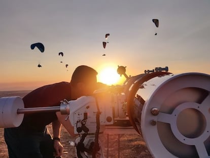 Un observador mira a través de un telescopio mientras otros practican parapente en la montaña de La Muela, en Alarilla (Guadalajara).