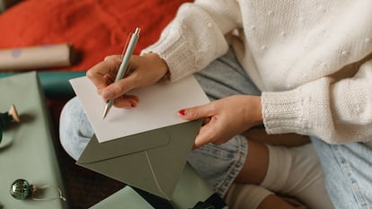 Una chica escribiendo una postal con un bolígrafo encima de su pierna.