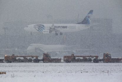 Un avión de las líneas aéreas egipcias aterriza durante una nevada en el aeropuerto de Fráncfort mientras dos máquinas quitanieves despejan otra pista.