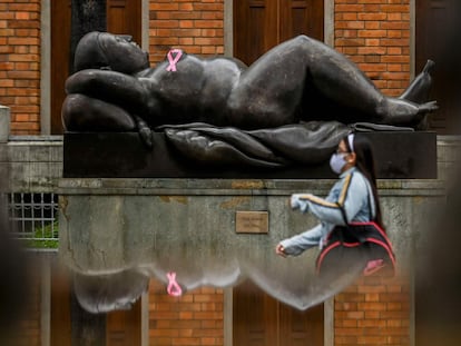 Una mujer pasa frente a una estatua con un lazo rosa, el símbolo del cáncer de mama.