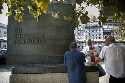 Un grupo de taxistas juegan a las cartas al lado de la estatua dedicada al emigrante portugu&eacute;s.