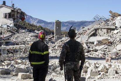 Dos miembros del personal de emergencias, de pie, ante varias ruinas en la localidad de Amatrice. En esta misma población, se dio un terremoto de magnitud 6, el pasado 24 de agosto, que provocó 297 muertos dejando a más de 2.500 personas sin hogar.