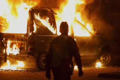 Un policía antidisturbios observa el incendio de un coche vandalizado por un grupo de manifestantes en la ciudad fronteriza de Estrasburgo.