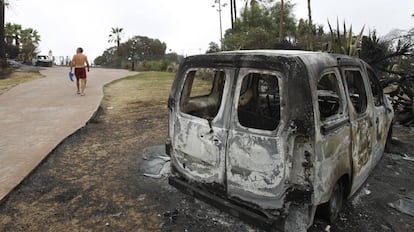 Un vecino de La Alcaidesa camina junto a un coche calcinado por el incendio de la Línea (Cádiz).