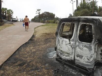 Un vecino de La Alcaidesa camina junto a un coche calcinado por el incendio de la Línea (Cádiz).