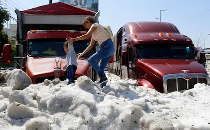 El granizo afectó a decenas de vehículos en Guadalajara, capital del estado de Jalisco, y dejó sepultados numerosos coches. En la imagen, una mujer camina junto a su hijo sobre una montaña de granizo.