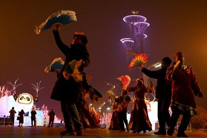 Residentes locales bailan en el Parque Olímpico, cerca de la Torre Olímpica de Pekín, China, iluminada por la noche.