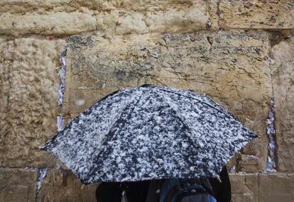 Un hombre sostiene un paraguas ante el Muro de las Lamentaciones. Tres centímetros de nieve cubren los tejados y calles de Jerusalén, donde la Alcaldía ha tenido que sacar a los vehículos municipales para que limpien las calzadas antes de que, a la caída del sol esta tarde, comience la jornada sagrada del Sabath, en la que los judíos creyentes no pueden realizar trabajos y la mayoría de los servicios públicos israelíes no funcionan.