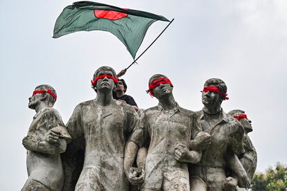 A Bangladeshi student waves his country's flag atop the Raju Memorial Sculpture during protests on Saturday 3.