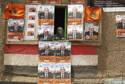 Una mujer asomada a una ventana rodeada de carteles del candidato Abulfutú en El Cairo.