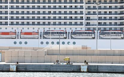 Un pescador se protege del sol de agosto en el puerto de Valencia, con un crucero a sus espaldas.