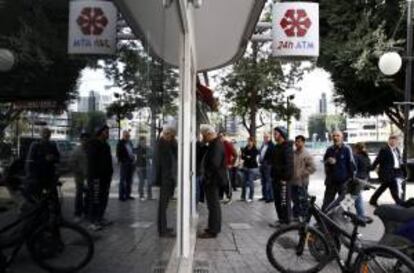 Un grupo de personas hace cola el pasado viernes junto al cajero automático de una sucursal cerrada del banco Laiki, en Nicosia, Chipre.